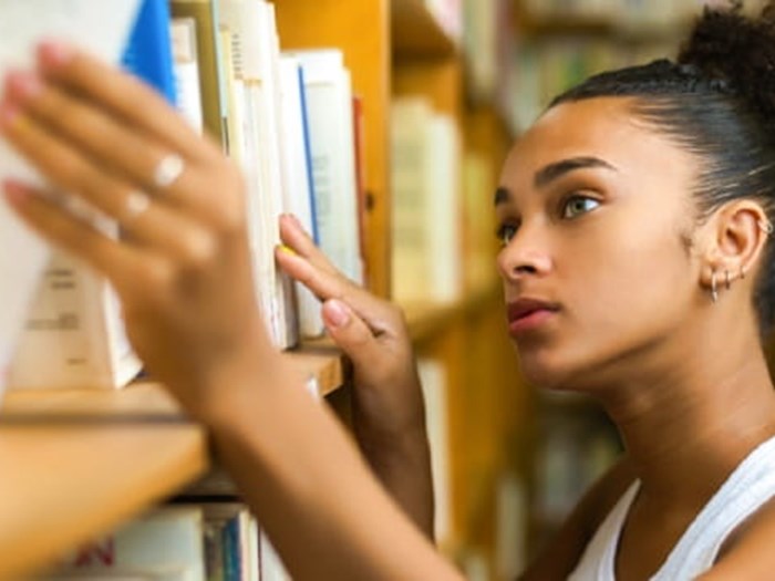 Young woman taking a book down from a library shelf