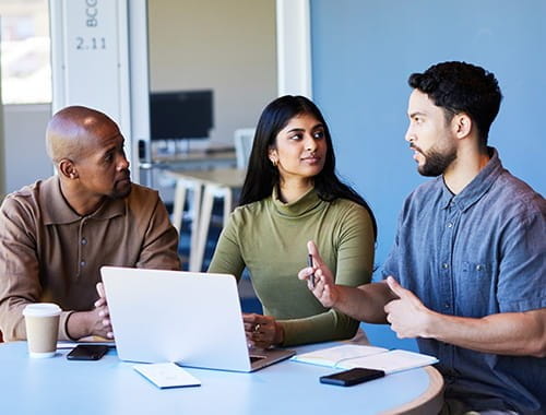 three colleagues students talking meeting office table laptop
