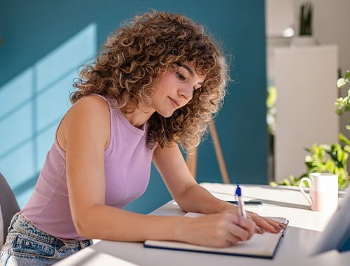 young woman student working studying in a home office writing pen paper desk