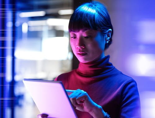 young asian woman holding using pointing at an electronic tablet in front of blurred blue lighting