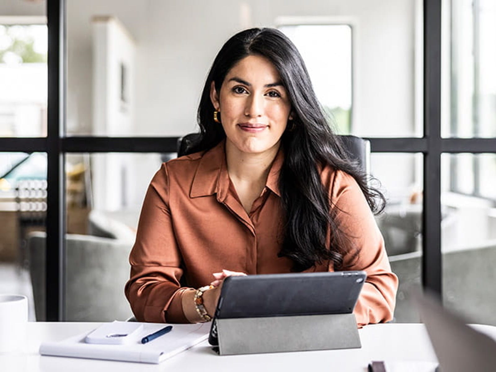 young woman smiling employee sitting in an office meeting room with a tablet pen paper glass walls