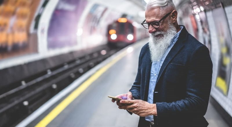 Mature man with grey beard checking phone at London Underground