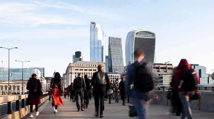 Commuters walking over London Bridge with the financial district in the background