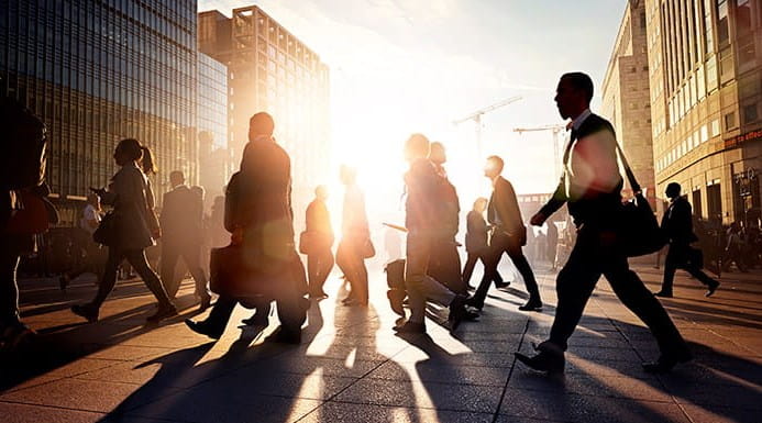 Silhouettes of commuters walking outside at dusk with buildings in the background