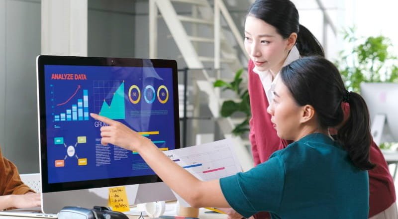 Two young women looking at charts on a computer monitor
