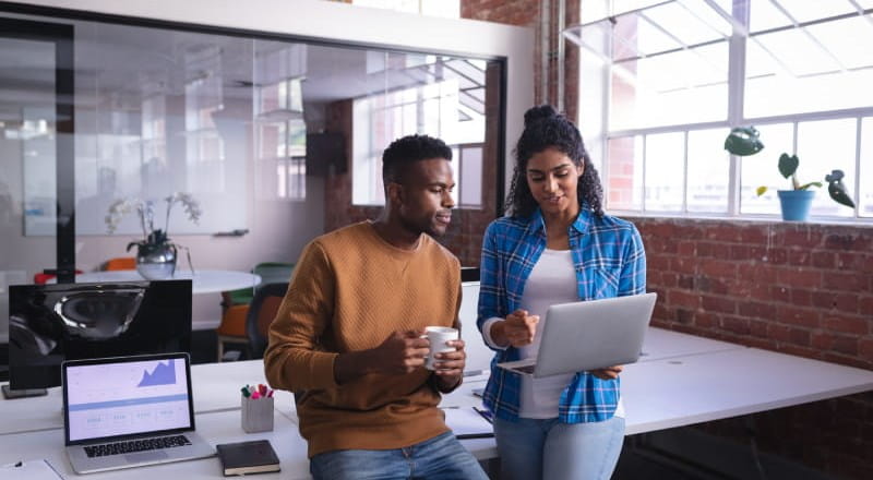 Casually dressed office workers looking at laptop while having coffee