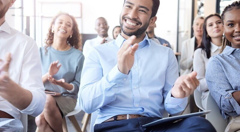 many employees clapping their hands and smiling.