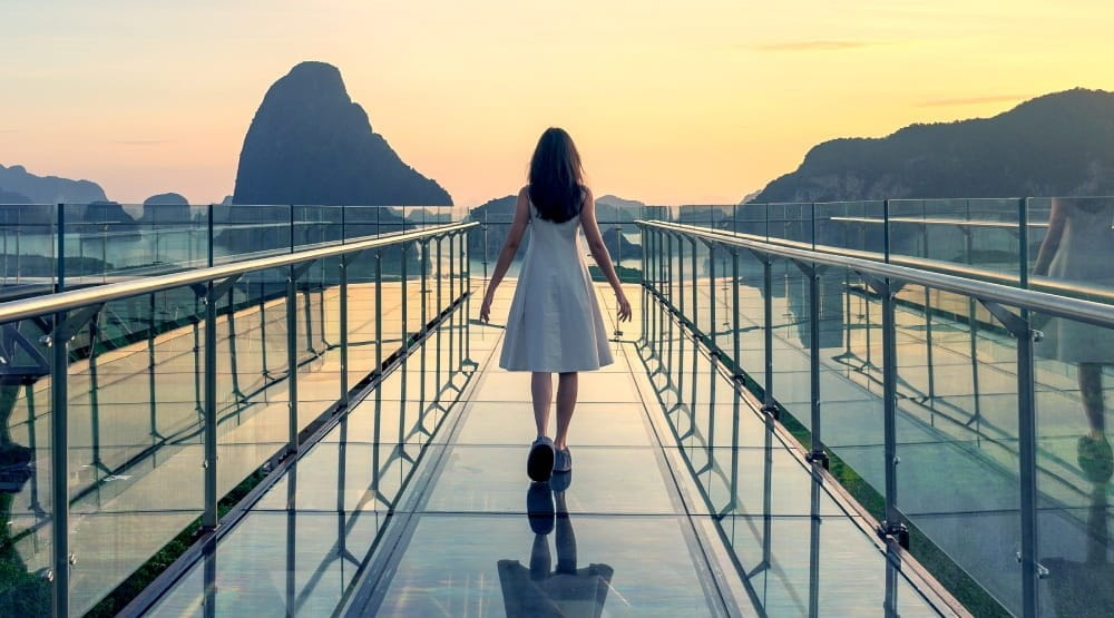 Woman walking over a glass bridge at sunset